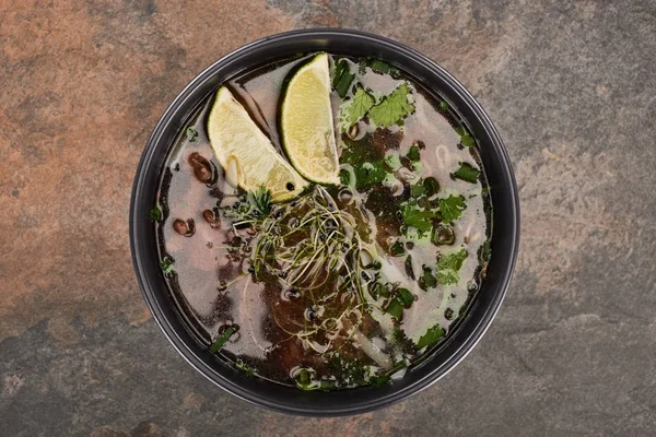 Vue du dessus du pho dans un bol avec de la lime et de la coriandre sur fond de pierre — Photo de stock