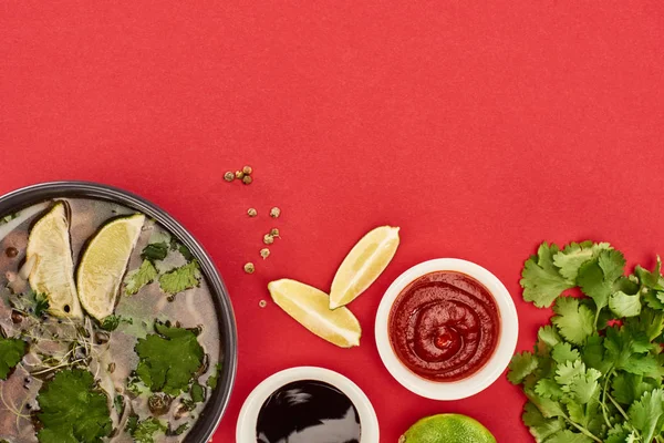 Top view of pho in bowl near lime, chili and soy sauces and coriander on red background — Stock Photo