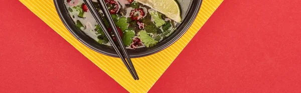 Vue du haut du pho dans un bol avec baguettes, lime, chili et coriandre sur fond rouge et jaune, panoramique — Photo de stock