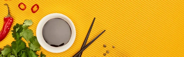 Top view of chili, soy sauce and coriander near chopsticks on yellow background, panoramic shot — Stock Photo