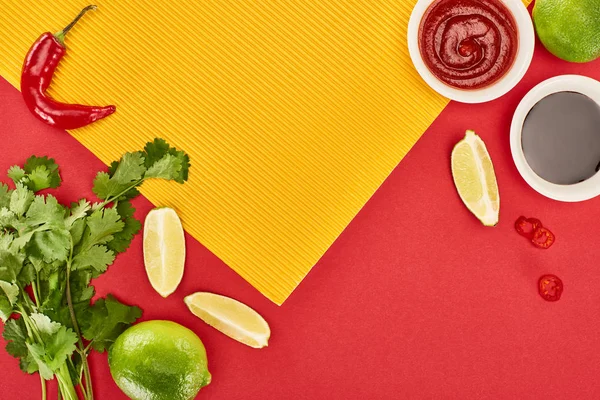 Top view of lime, chili and soy sauces and coriander on red and yellow background — Stock Photo