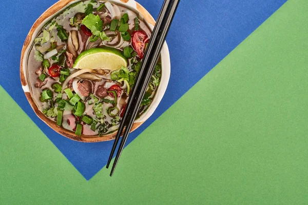 Верхний вид фо в миске с палочками для еды на синем и зеленом фоне — стоковое фото