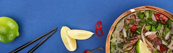 Draufsicht auf Pho in Schale in der Nähe von Essstäbchen, Limette, Chili auf blauem Hintergrund, Panoramaaufnahme — Stockfoto