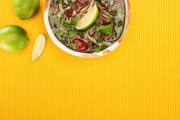 Top view of pho in bowl near lime on yellow textured background — Stock Photo