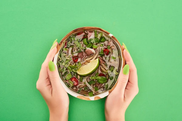 Cropped view of woman holding pho in bowl on green background — Stock Photo