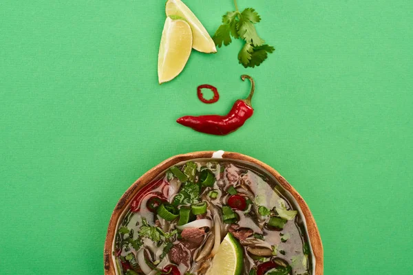 Top view of pho in bowl near lime, chili and coriander on green background — Stock Photo