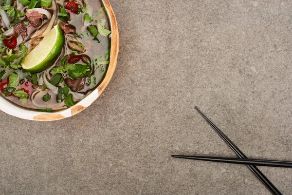 Top view of pho in bowl near chopsticks on grey background — Stock Photo