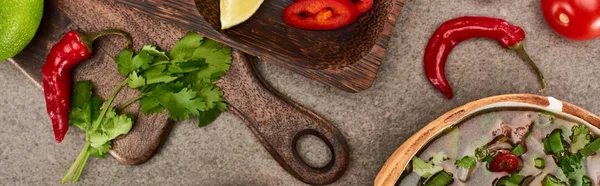 Vista superior de pho en tazón cerca de cal, chile y cilantro sobre tabla de cortar de madera sobre fondo gris, plano panorámico — Stock Photo