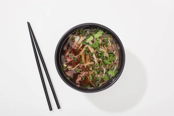 Top view of pho in bowl near chopsticks on white background — Stock Photo