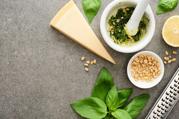 Vista superior de la salsa de pesto ingredientes crudos y utensilios de cocina en la superficie gris - foto de stock