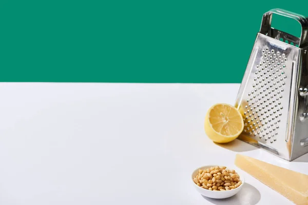 Lemon, parmesan, pine nuts and grater on white table isolated on green — Stock Photo