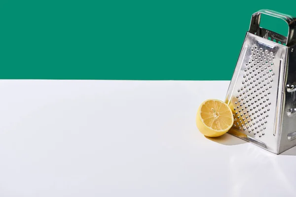 Lemon and grater on white table isolated on green — Stock Photo