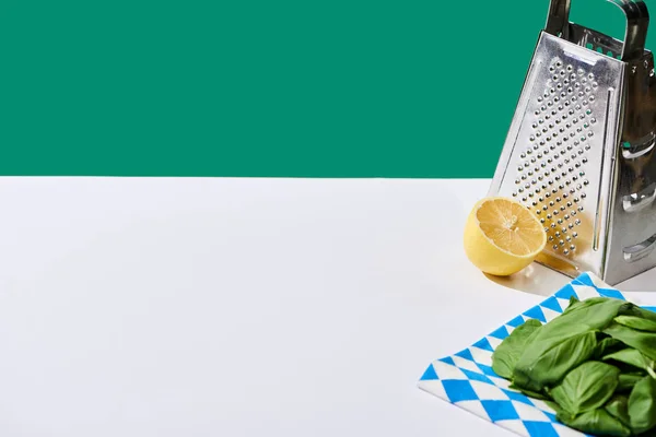 Lemon, basil leaves and grater on white table isolated on green — Stock Photo
