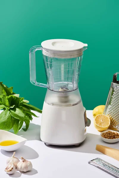 Pesto sauce raw ingredients and food processor on white table isolated on green — Stock Photo