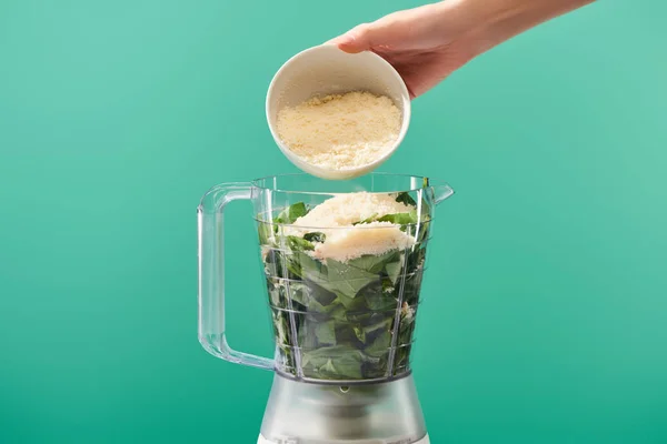 Cropped view of woman adding grated Parmesan to basil leaves in food processor isolated on green — Stock Photo