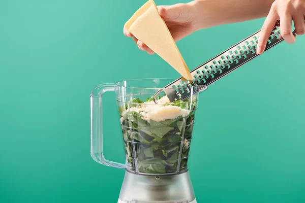 Vista ritagliata di donna grattugia parmigiano nel robot da cucina con foglie di basilico isolato su verde — Foto stock
