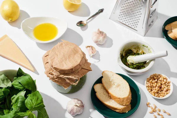 Molho pesto perto de ingredientes, ralador e pão no fundo branco — Fotografia de Stock