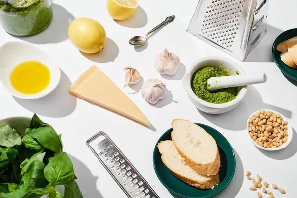 Molho pesto perto de ingredientes, raladores e pão sobre fundo branco — Fotografia de Stock