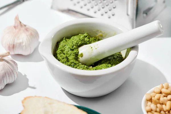 Nahaufnahme von Pesto-Sauce in Pounder in der Nähe der Reibe, Brot und Zutaten auf weißem Hintergrund — Stockfoto
