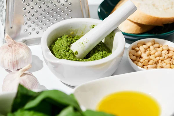 Primer plano vista de salsa de pesto en cucharón cerca rallador, pan e ingredientes sobre fondo blanco - foto de stock