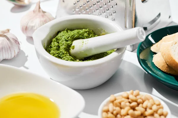 Primer plano vista de salsa de pesto en cucharón cerca rallador, pan e ingredientes sobre fondo blanco - foto de stock