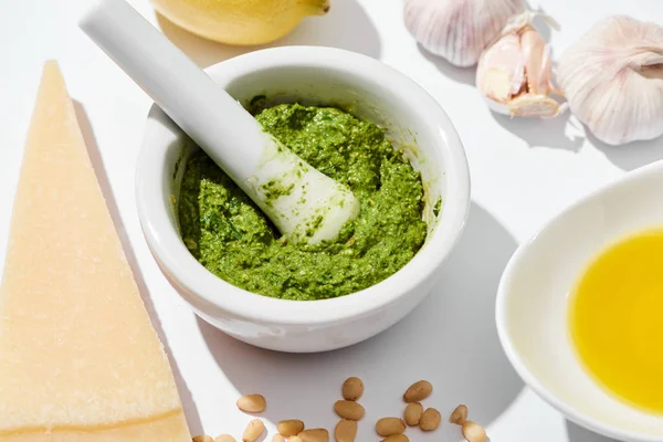 Close up view of pesto sauce in pounder near ingredients on white background — Stock Photo