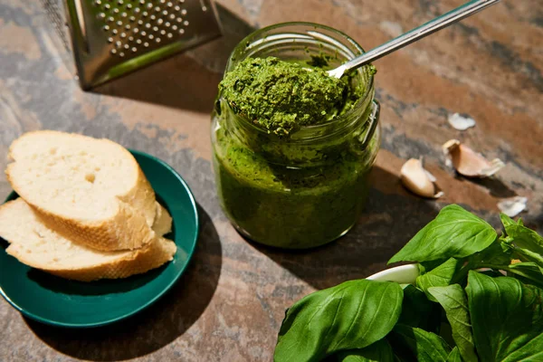 Baguette slices, pesto sauce in jar, grater and fresh ingredients on stone surface — Stock Photo
