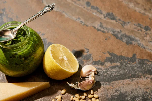 Pesto sauce in glass jar with spoon near ingredients on stone surface — Stock Photo