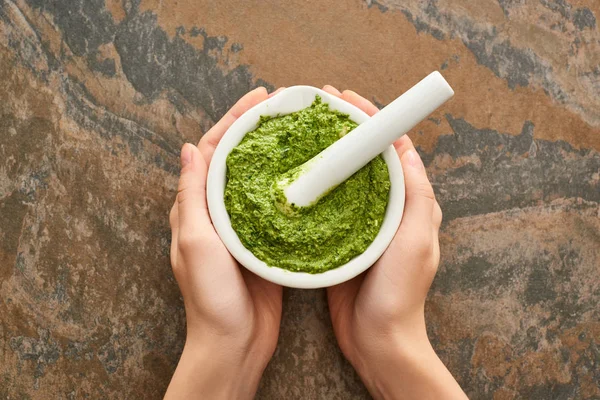 Vista recortada de la mujer sosteniendo tazón con salsa de pesto en la superficie de piedra - foto de stock