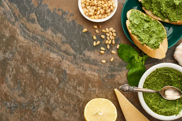 Blick von oben auf Baguette-Scheiben mit Pesto-Sauce auf Teller in der Nähe frischer Zutaten auf Steinoberfläche — Stockfoto