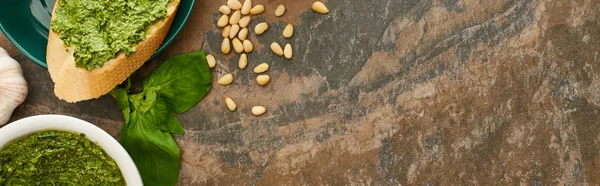 Vue de dessus de la tranche de baguette avec sauce pesto sur assiette près des ingrédients frais sur la surface de la pierre, vue panoramique — Photo de stock