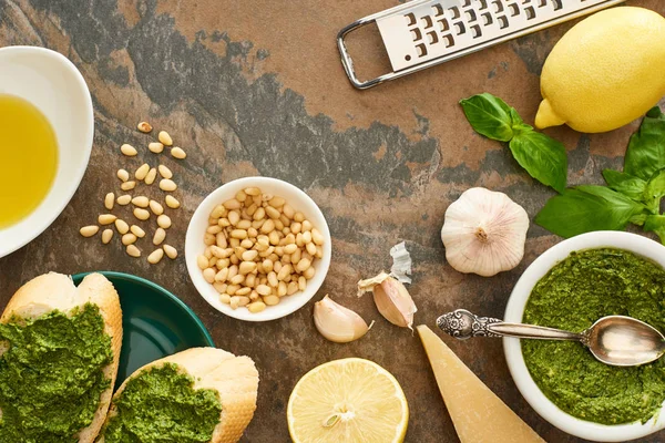 Vista dall'alto di fette di baguette con salsa di pesto su piatto vicino a ingredienti freschi e utensili da cucina su superficie di pietra — Foto stock