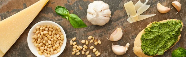 Vista superior de fatia de baguete com molho de pesto perto de ingredientes frescos na superfície de pedra, tiro panorâmico — Fotografia de Stock