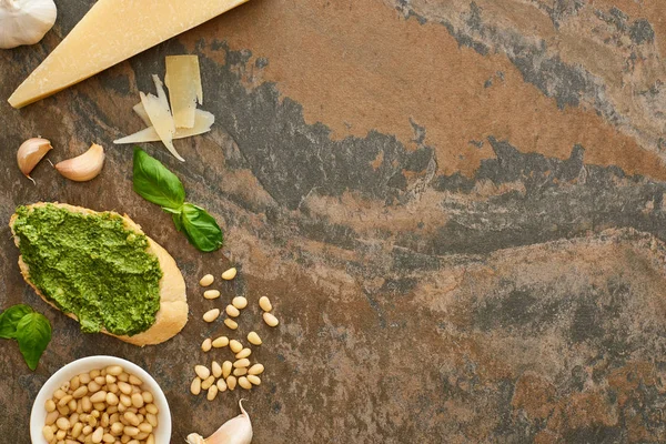 Vista superior da fatia de baguete com molho de pesto perto de ingredientes frescos na superfície de pedra — Fotografia de Stock