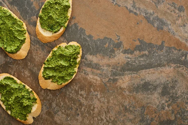 Blick von oben auf Baguette-Scheiben mit köstlicher Pesto-Sauce auf Steinoberfläche — Stockfoto