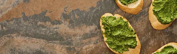 Vue de dessus des tranches de baguette avec délicieuse sauce pesto sur la surface en pierre, vue panoramique — Photo de stock