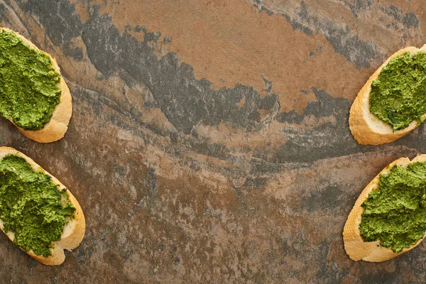 Vue de dessus des tranches de baguette avec délicieuse sauce pesto sur la surface de la pierre — Photo de stock