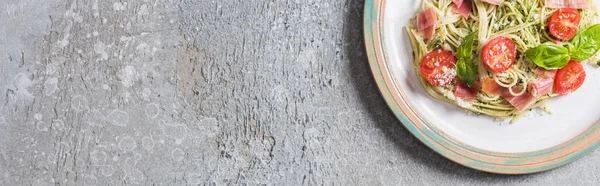 Top view of cooked Pappardelle with tomatoes, basil and prosciutto on plate on grey surface, panoramic shot — Stock Photo