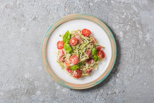 Draufsicht auf gekochte Pappardelle mit Tomaten, Basilikum und Schinken auf Teller auf grauer Oberfläche — Stockfoto