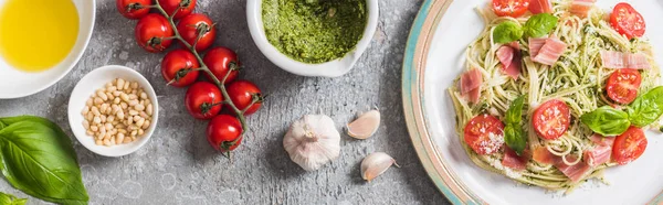 Vue du dessus de la Pappardelle cuite aux tomates, basilic et prosciutto près des ingrédients sur la surface grise, vue panoramique — Photo de stock