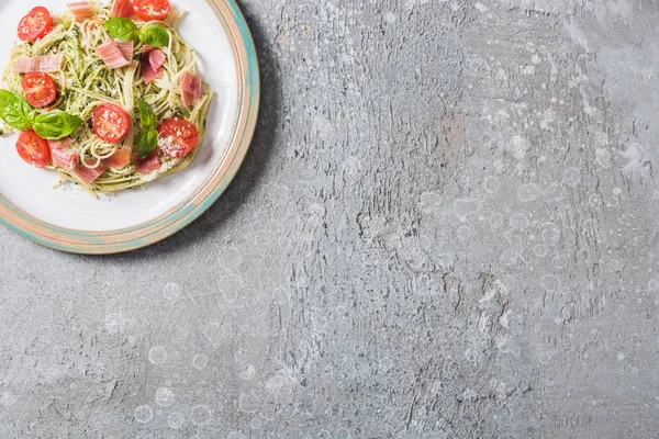 Top view of cooked Pappardelle with tomatoes, basil and prosciutto on plate on grey surface — Stock Photo