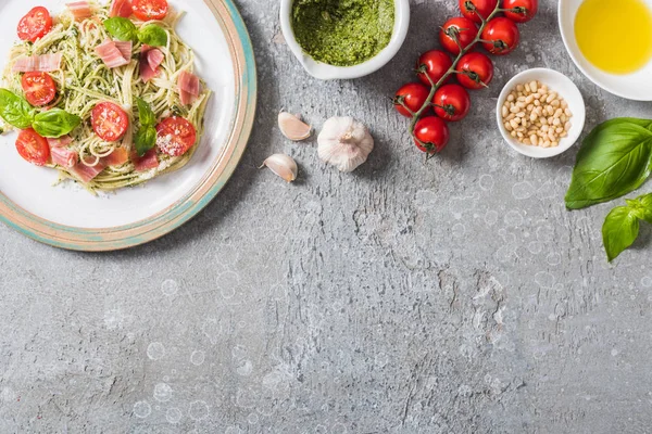 Vue du dessus de la Pappardelle cuite avec tomates, basilic et prosciutto près des ingrédients sur la surface grise — Photo de stock