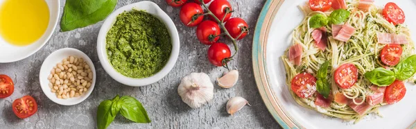 Vista dall'alto delle Pappardelle cotte con pomodori, basilico e prosciutto in prossimità di ingredienti su superficie grigia, colpo panoramico — Foto stock