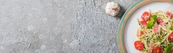 Vista dall'alto delle Pappardelle cotte con pomodori, basilico e prosciutto vicino all'aglio su superficie grigia, colpo panoramico — Foto stock