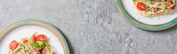 Top view of Pappardelle with tomatoes, basil and prosciutto on plates on grey surface, panoramic shot — Stock Photo