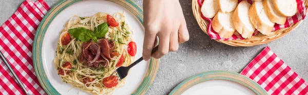 Vista cortada de mulher comer Pappardelle com tomates, manjericão e prosciutto perto baguete na superfície cinza, tiro panorâmico — Fotografia de Stock