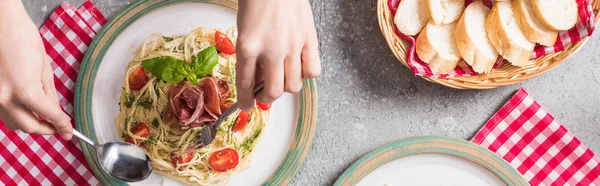 Vista cortada de mulher comer Pappardelle com tomates, manjericão e prosciutto perto baguete na superfície cinza, tiro panorâmico — Fotografia de Stock