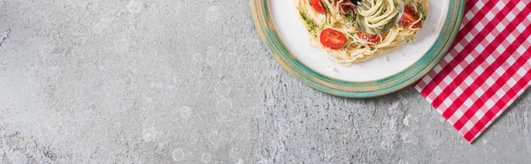 Top view of served Pappardelle with tomatoes, basil and prosciutto on plaid napkin on grey surface, panoramic shot — Stock Photo