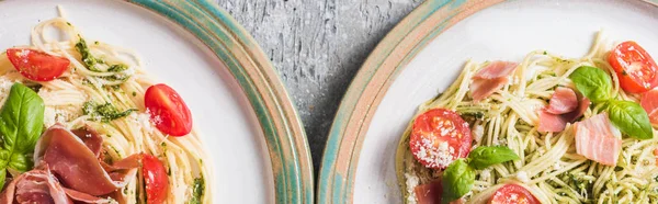 Top view of cooked Pappardelle with tomatoes, basil and prosciutto on plates on grey surface, panoramic shot — Stock Photo