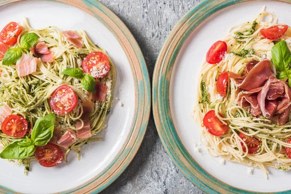 Draufsicht auf gekochte Pappardelle mit Tomaten, Basilikum und Schinken auf Tellern auf grauer Oberfläche — Stockfoto